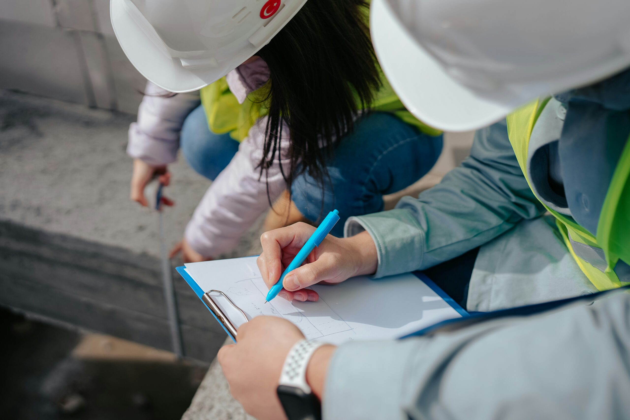Two experts in hard hats inspecting a property with plans before buying a lakefront cottage